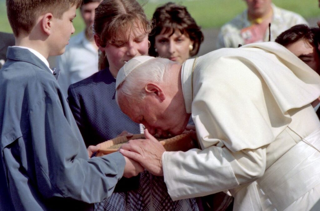 Papež Janez Pavel II. poljublja slovensko zemljo. Zemlja je v glineni skledi, ki jo držita fant in dekle.