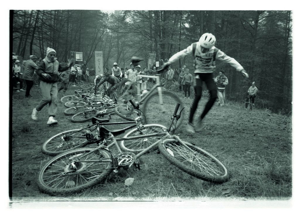 Kolesa položena na tla in kolesar v kolesarski opravi, ki drži kolo.