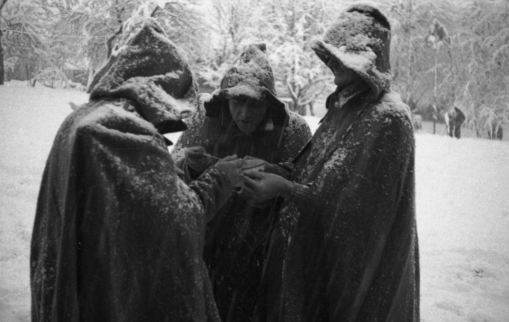 Trije moški v plaščih s kapuco.