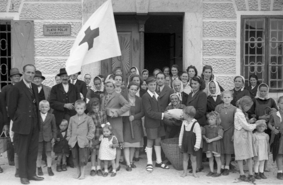 Skupinska fotografija žensk, otrok in moških pred poslopjem.