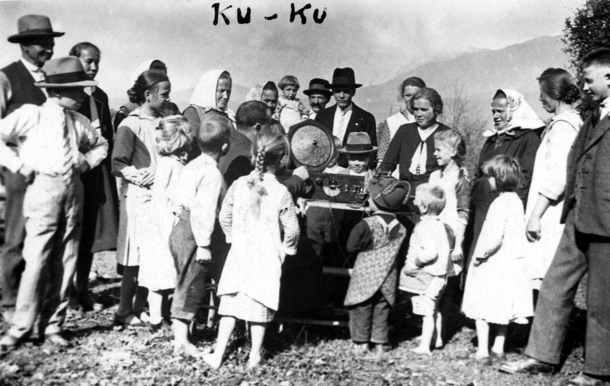 Odrasli in otroci stojijo zunaj okrog radia